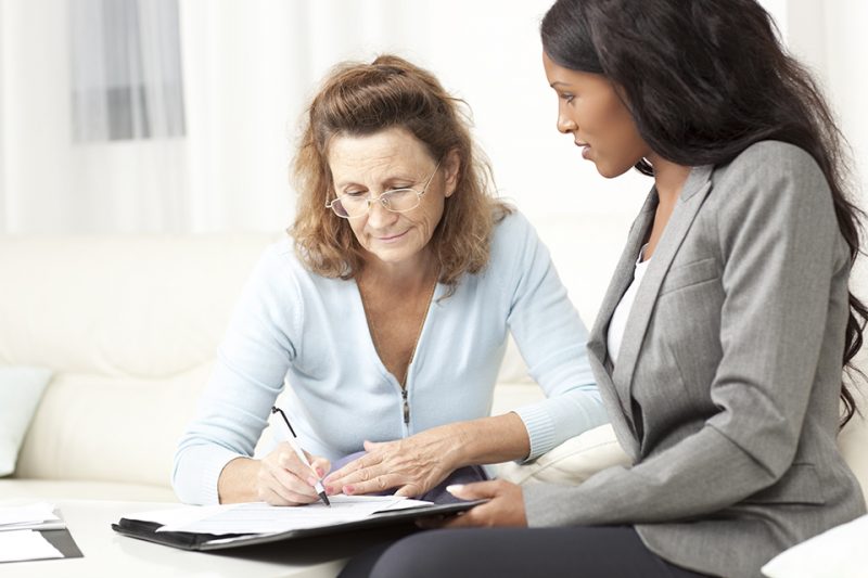 Senior woman meeting with financial advisor at home. Woman signs a document that has been brought to her by her personal assistant.